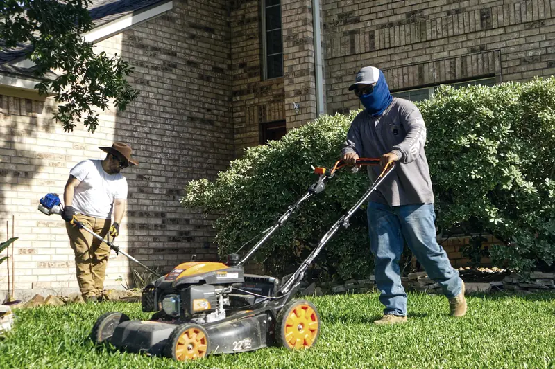Two landscapers mowing and trimming a residential lawn