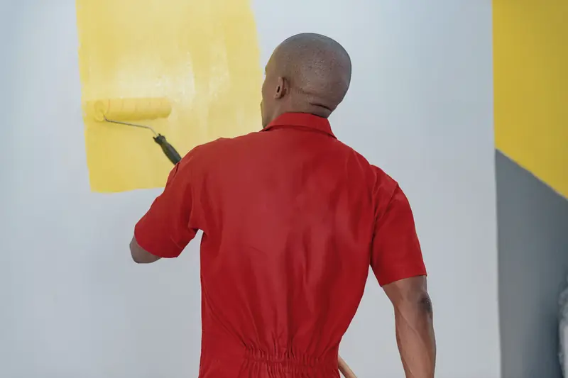 Painter rolling yellow paint onto an interior wall